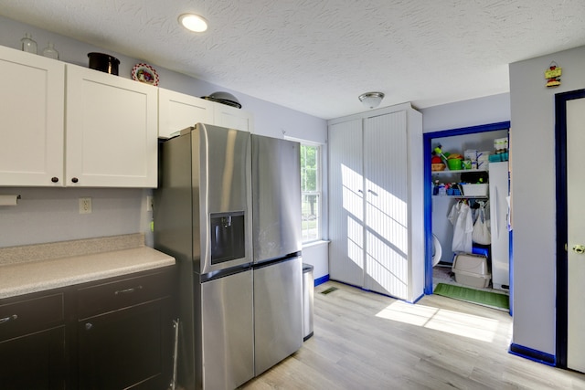 kitchen with stainless steel fridge, a textured ceiling, white cabinets, and light hardwood / wood-style floors