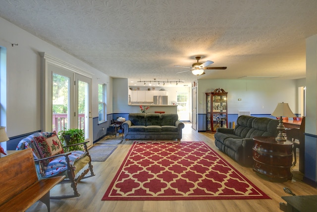 living room with a textured ceiling, french doors, rail lighting, ceiling fan, and light wood-type flooring