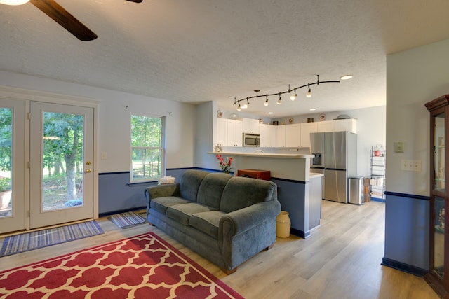 living room featuring a textured ceiling, rail lighting, ceiling fan, and light wood-type flooring