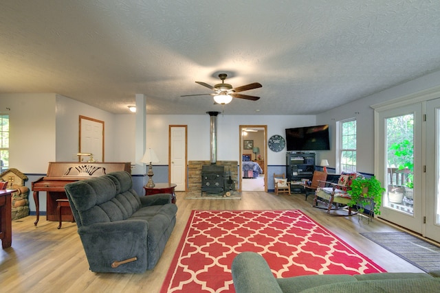 living room with a textured ceiling, light hardwood / wood-style flooring, ceiling fan, and a wood stove