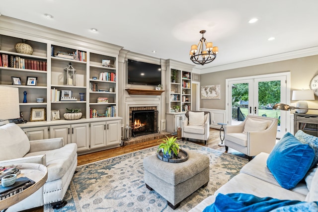 living room with wood-type flooring, ornamental molding, a brick fireplace, and a notable chandelier