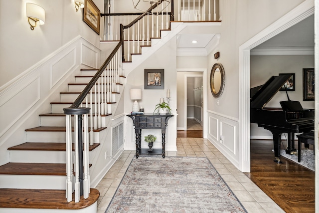 entryway with a towering ceiling, ornamental molding, and light hardwood / wood-style flooring