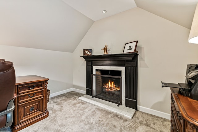 carpeted home office with a tile fireplace and vaulted ceiling