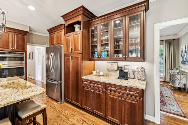 kitchen with crown molding, light hardwood / wood-style flooring, light stone counters, appliances with stainless steel finishes, and a breakfast bar area