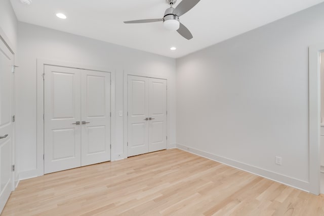 unfurnished bedroom with ceiling fan, light hardwood / wood-style floors, and two closets