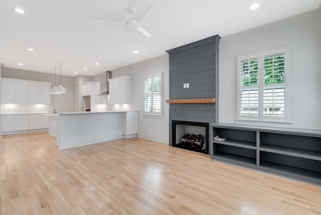 unfurnished living room featuring crown molding, a fireplace, ceiling fan, and light wood-type flooring