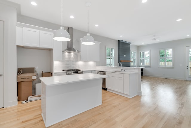 kitchen featuring white cabinetry, stainless steel appliances, wall chimney range hood, kitchen peninsula, and pendant lighting