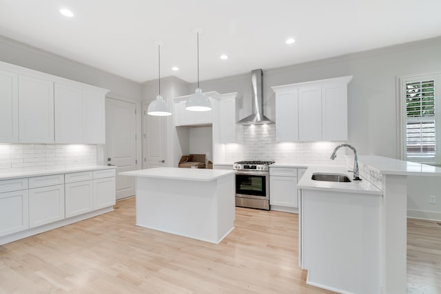 kitchen with gas stove, sink, hanging light fixtures, wall chimney range hood, and a kitchen island