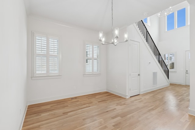 unfurnished dining area with a healthy amount of sunlight, light hardwood / wood-style floors, ornamental molding, and a chandelier