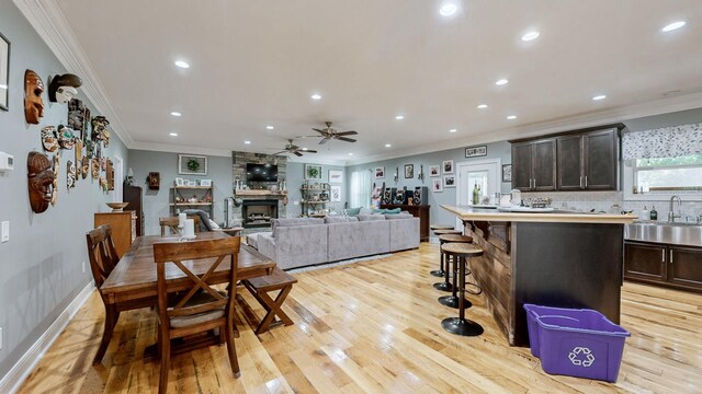 dining area featuring a fireplace, ceiling fan, sink, and light wood-type flooring