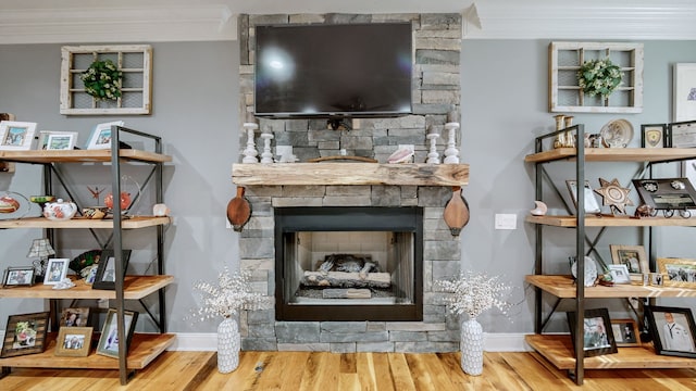 living room with wood-type flooring, crown molding, and a stone fireplace