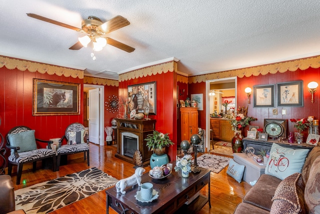 living room featuring ornamental molding, a fireplace, hardwood / wood-style flooring, a textured ceiling, and ceiling fan