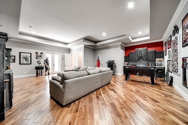 living room featuring light hardwood / wood-style flooring, crown molding, a raised ceiling, and a barn door