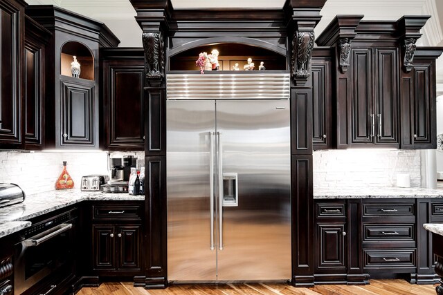 kitchen with appliances with stainless steel finishes, light stone counters, light hardwood / wood-style floors, and tasteful backsplash