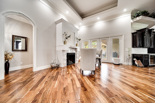 living room with light wood-type flooring, a tray ceiling, a towering ceiling, wine cooler, and a premium fireplace