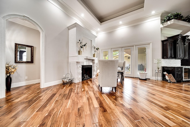 living room with light wood-type flooring, a high end fireplace, beverage cooler, and crown molding