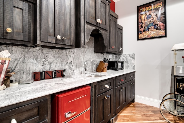 kitchen with backsplash, light hardwood / wood-style floors, light stone countertops, sink, and dark brown cabinets