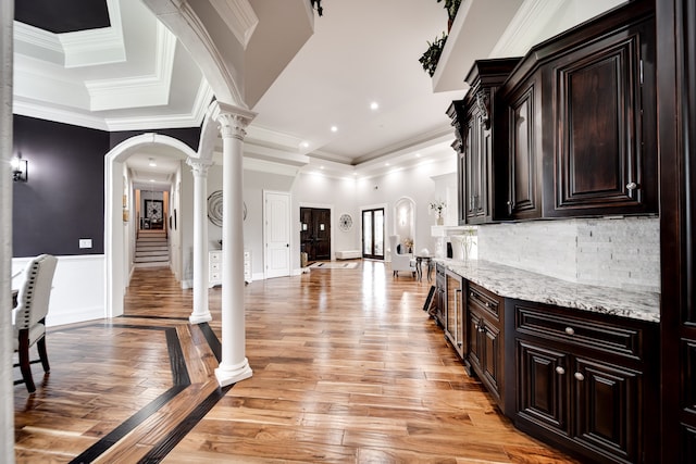 kitchen featuring ornate columns, light wood-type flooring, light stone countertops, tasteful backsplash, and a raised ceiling