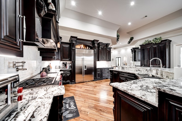 kitchen featuring tasteful backsplash, light wood-style flooring, light stone countertops, stainless steel appliances, and a sink