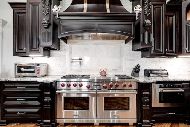 kitchen with appliances with stainless steel finishes, a toaster, light stone counters, and custom exhaust hood