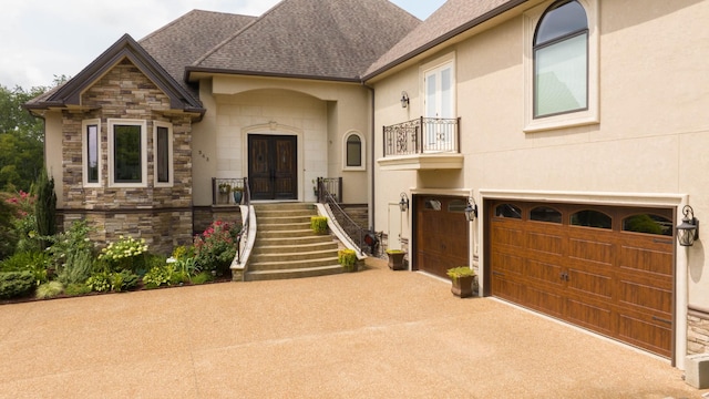 view of front of property featuring french doors, a shingled roof, an attached garage, stone siding, and driveway