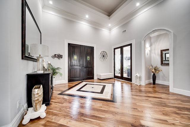 foyer entrance with a high ceiling, hardwood / wood-style floors, ornamental molding, and french doors