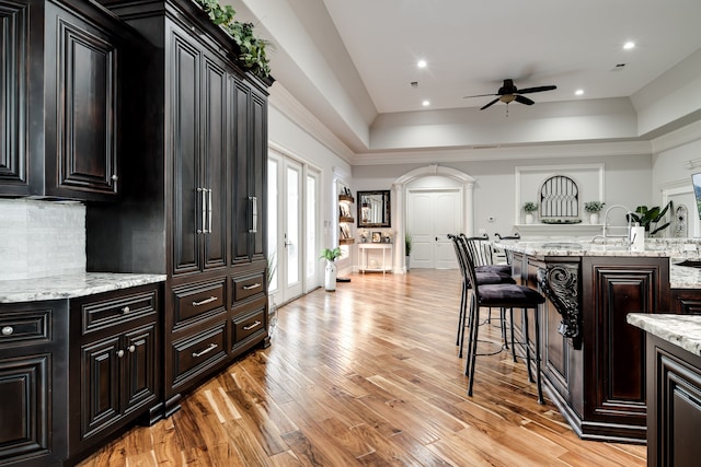 kitchen featuring ceiling fan, a kitchen bar, light hardwood / wood-style flooring, and a tray ceiling