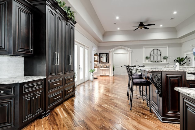 kitchen with a tray ceiling, tasteful backsplash, light wood-style flooring, dark cabinets, and a kitchen bar