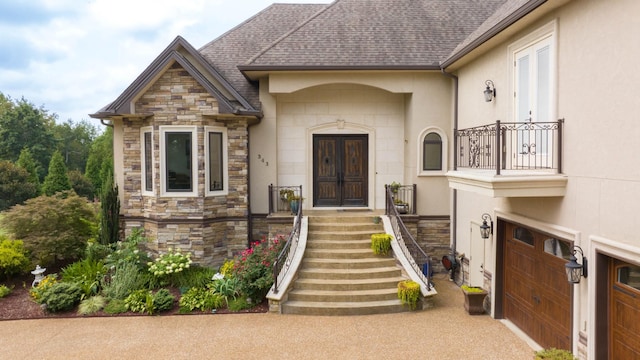 doorway to property with an attached garage, a shingled roof, stone siding, french doors, and driveway