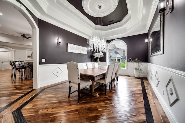 dining space featuring arched walkways, a wainscoted wall, a raised ceiling, visible vents, and hardwood / wood-style floors