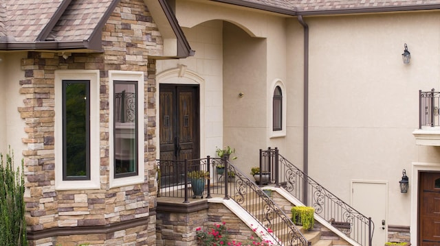 entrance to property with stone siding, a shingled roof, and stucco siding