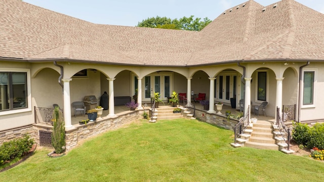 rear view of property featuring french doors, roof with shingles, stucco siding, a porch, and a lawn