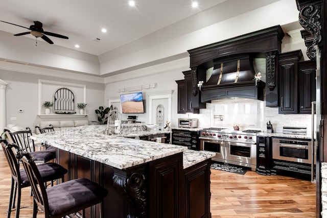 kitchen featuring backsplash, stainless steel appliances, light hardwood / wood-style floors, ceiling fan, and custom exhaust hood