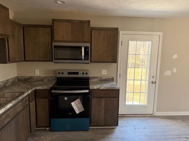 kitchen with appliances with stainless steel finishes, light wood-type flooring, a textured ceiling, and sink