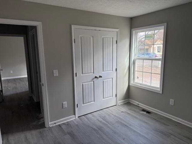 unfurnished bedroom with baseboards, visible vents, wood finished floors, a textured ceiling, and a closet