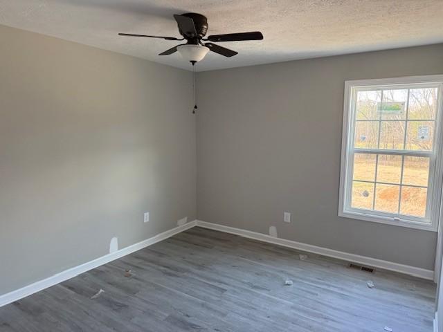 unfurnished room with a textured ceiling, dark wood-type flooring, visible vents, a ceiling fan, and baseboards