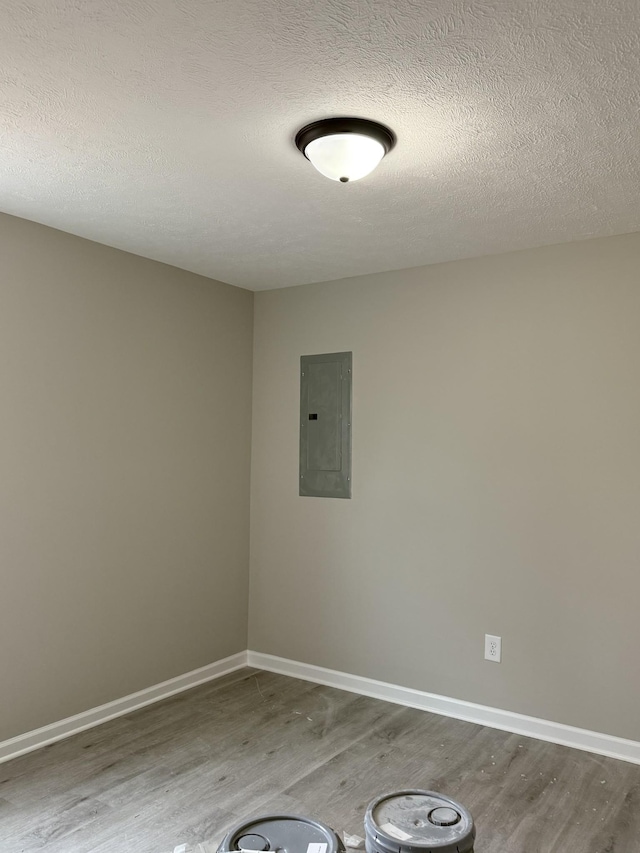 unfurnished room with electric panel, a textured ceiling, baseboards, and wood finished floors