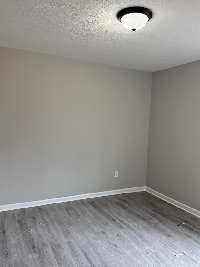 empty room featuring a textured ceiling, baseboards, and wood finished floors