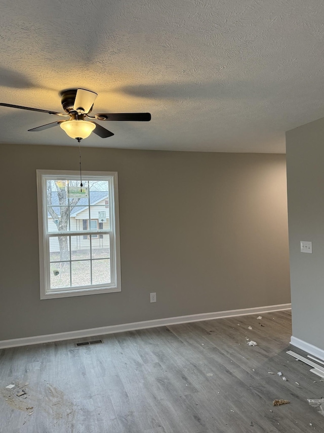 unfurnished room with a textured ceiling, wood finished floors, visible vents, and baseboards