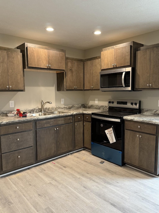 kitchen featuring light wood-type flooring, dark brown cabinetry, appliances with stainless steel finishes, and a sink