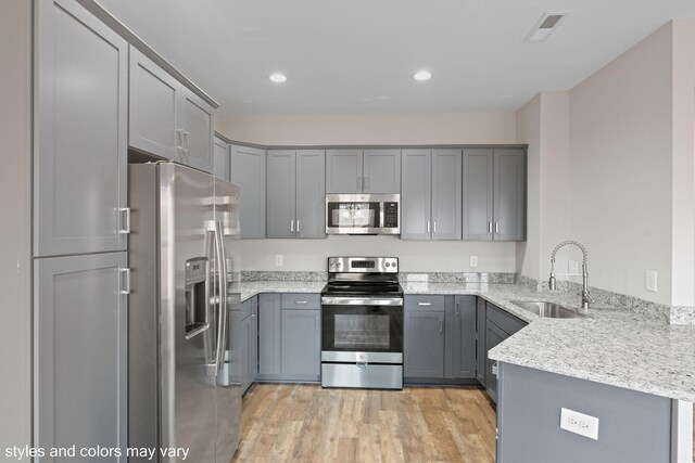 kitchen with sink, gray cabinets, light stone countertops, appliances with stainless steel finishes, and light hardwood / wood-style floors