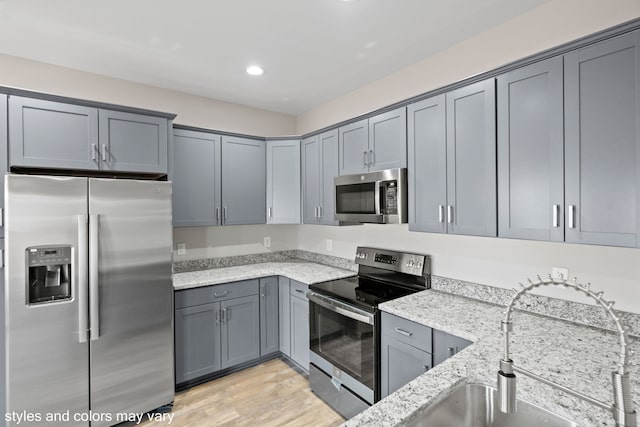 kitchen with appliances with stainless steel finishes, light wood-type flooring, gray cabinets, and light stone counters