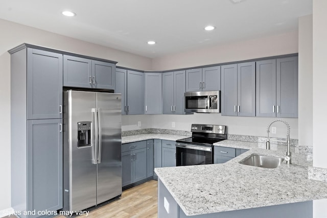 kitchen featuring light wood-type flooring, light stone countertops, sink, and appliances with stainless steel finishes