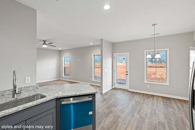 kitchen with light stone countertops, ceiling fan with notable chandelier, sink, dishwasher, and hanging light fixtures