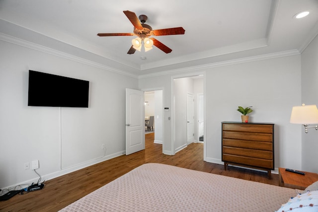 bedroom featuring a tray ceiling, a ceiling fan, ornamental molding, wood finished floors, and baseboards