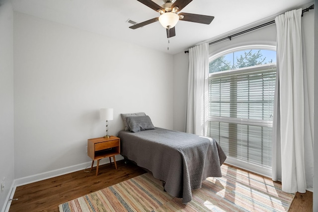 bedroom with ceiling fan, wood finished floors, visible vents, and baseboards