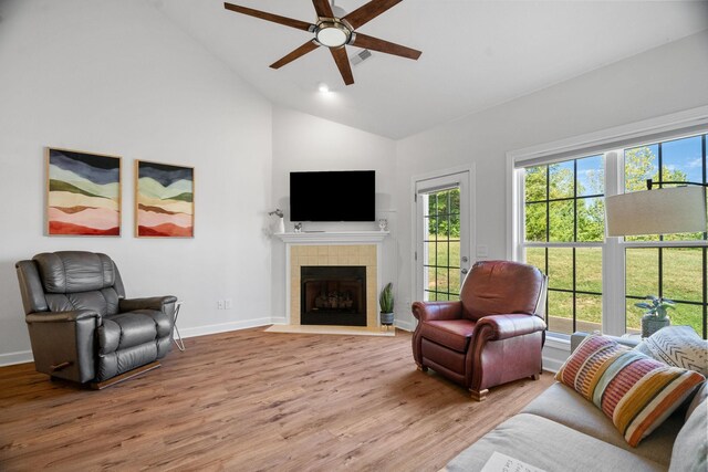 living room with ceiling fan, high vaulted ceiling, light hardwood / wood-style flooring, and a tiled fireplace