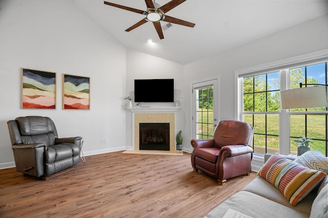 living area with high vaulted ceiling, a tile fireplace, baseboards, and wood finished floors