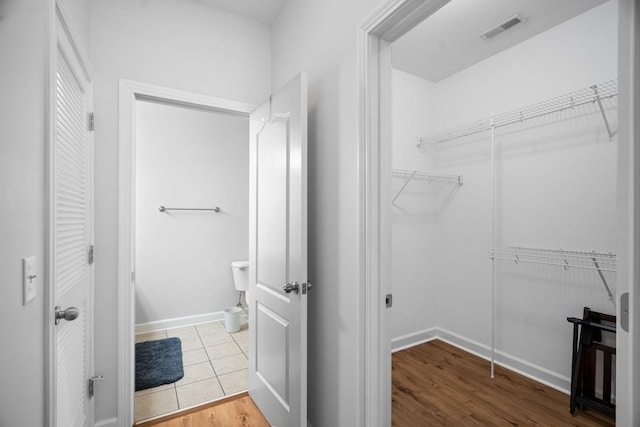 bathroom with baseboards, visible vents, toilet, wood finished floors, and a spacious closet