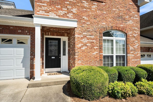 doorway to property featuring brick siding, roof with shingles, and an attached garage